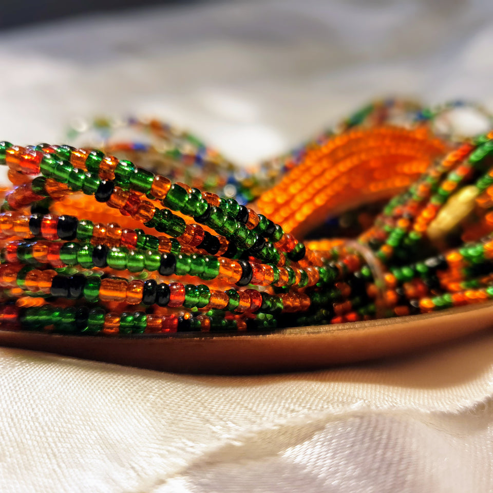 Close up image of waist beads in the colour of the Zambian flag place on a copper dish. Green, black, red and copper orange to celebrate Zambia and African Waistbeads